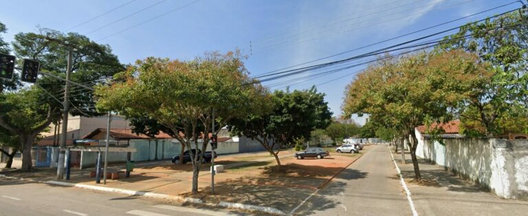 Panoramic view of the bus stop on Avenida Ouro Fino in São José dos Campos, with trees and a quiet residential street in the background under a clear sky.